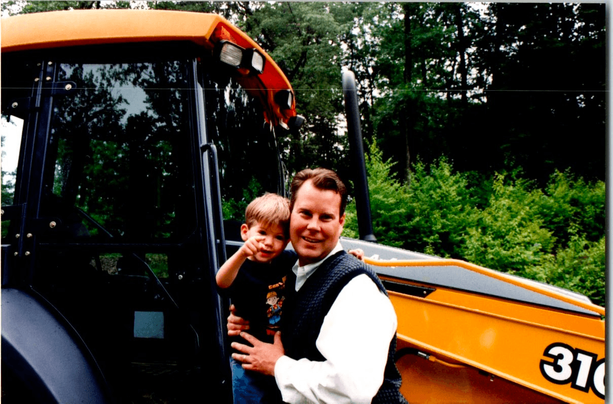 Dad and me next to a Caterpillar 310 backhoe on a job site