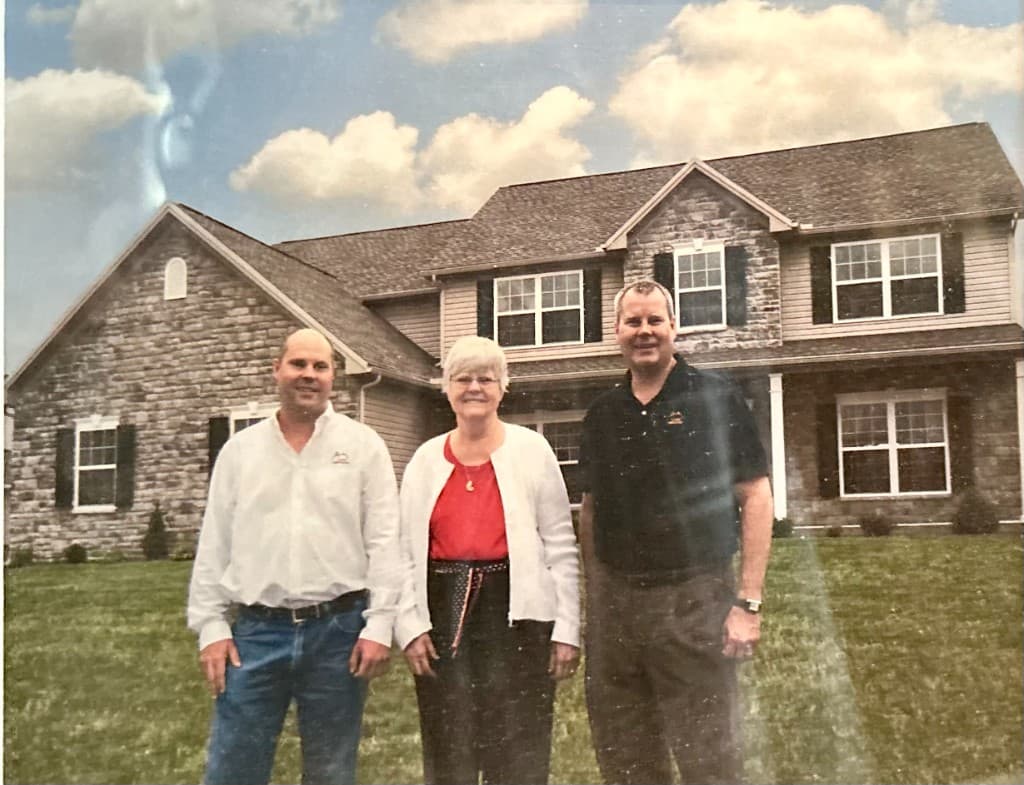 Jim Halbert, Virginia Halbert, and Doug Halbert standing together in front of a stone-and-siding Classic home