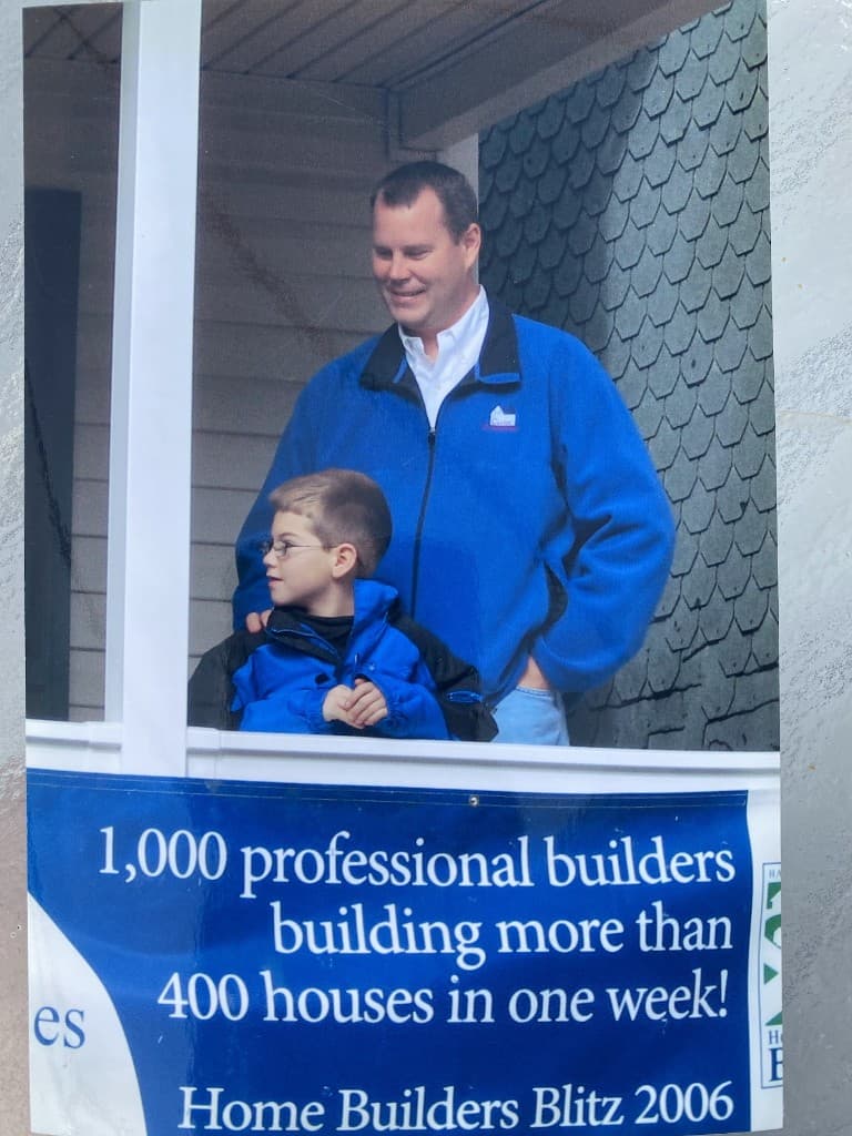 Doug Halbert and his son in front of a Home Builders Blitz 2006 banner at a Habitat for Humanity build