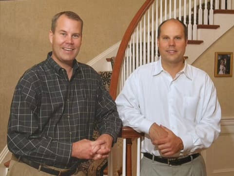Jim Halbert and Doug Halbert standing together at the foot of a curved staircase